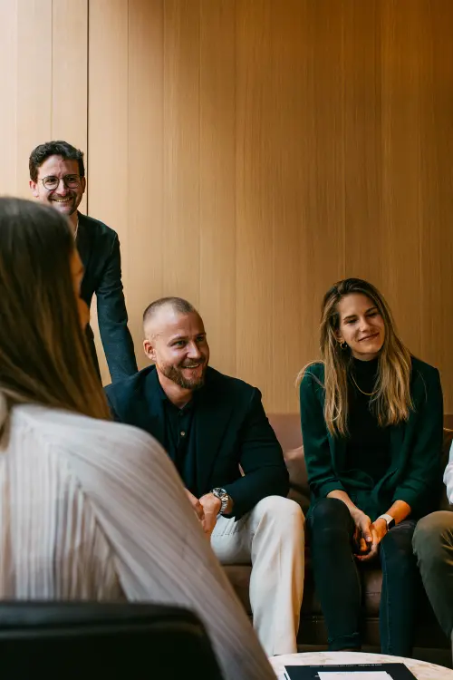 Teamgespräch im Lounge-Bereich – drei Mitarbeitende im Fokus, zwei weitere im Vordergrund unscharf