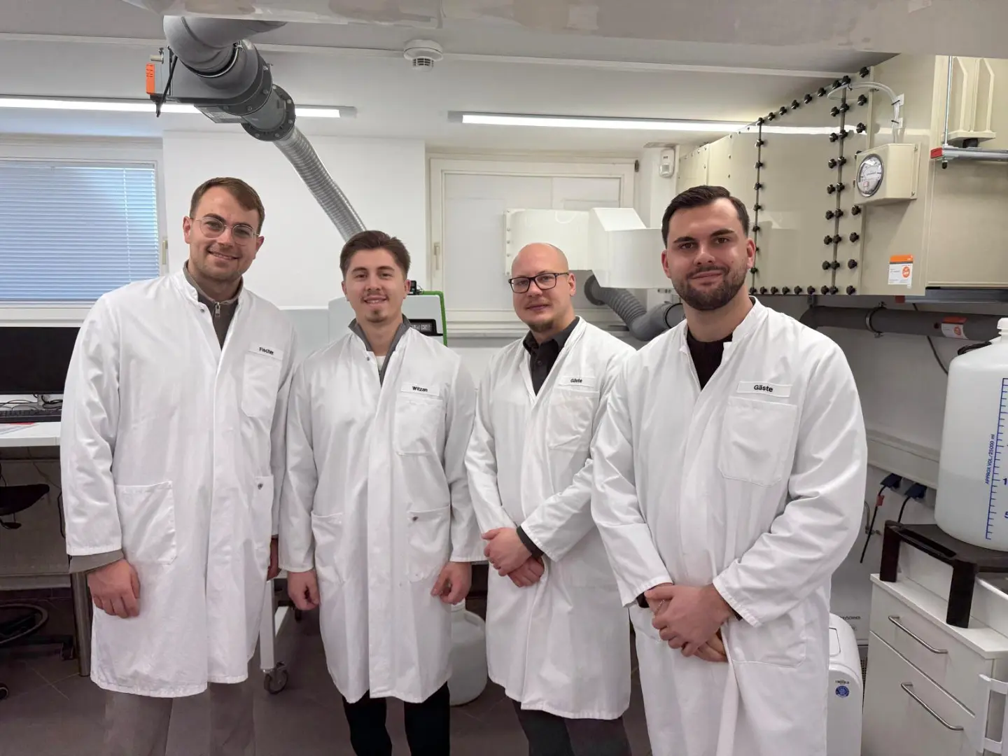 Vier Mitarbeiter des LPE Technik-Teams in weißen Laborkitteln stehen nebeneinander in einem Wasserlabor mit modernen Analysegeräten im Hintergrund